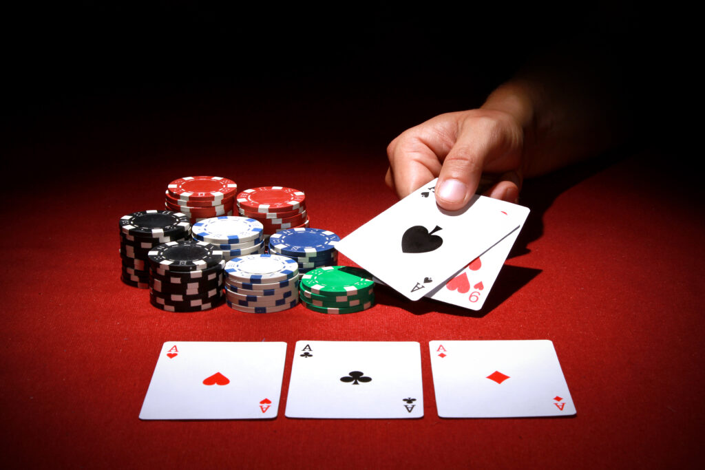 A photo of playing cards and casino chips on a table, with a person's hand holding two additional cards.