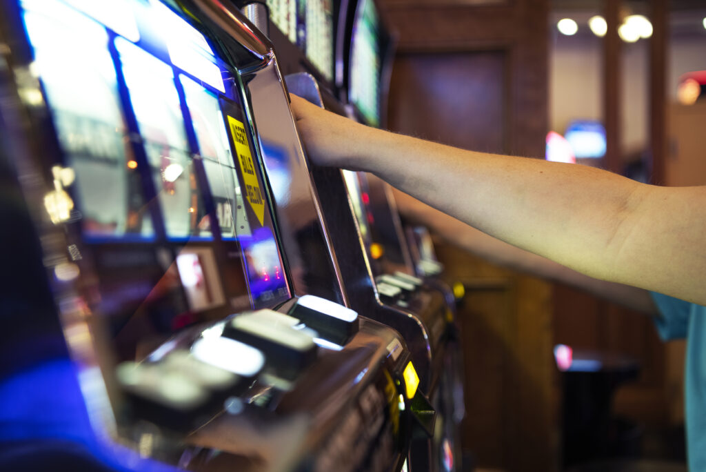 People playing slot machines in a casino (only arms in frame).