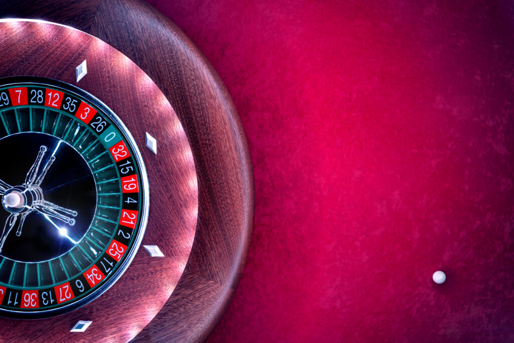 Close up of a roulette wheel with a roulette ball beside it on the red felt.