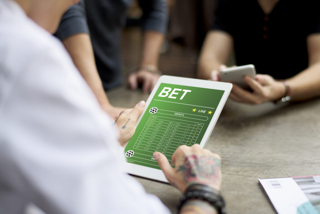 Man, mostly out a frame, holding a tablet showing a betting website.
