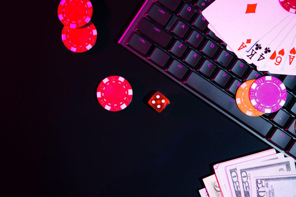 Casino chips, money, playing cards and a die on a black background and a computer keyboard.